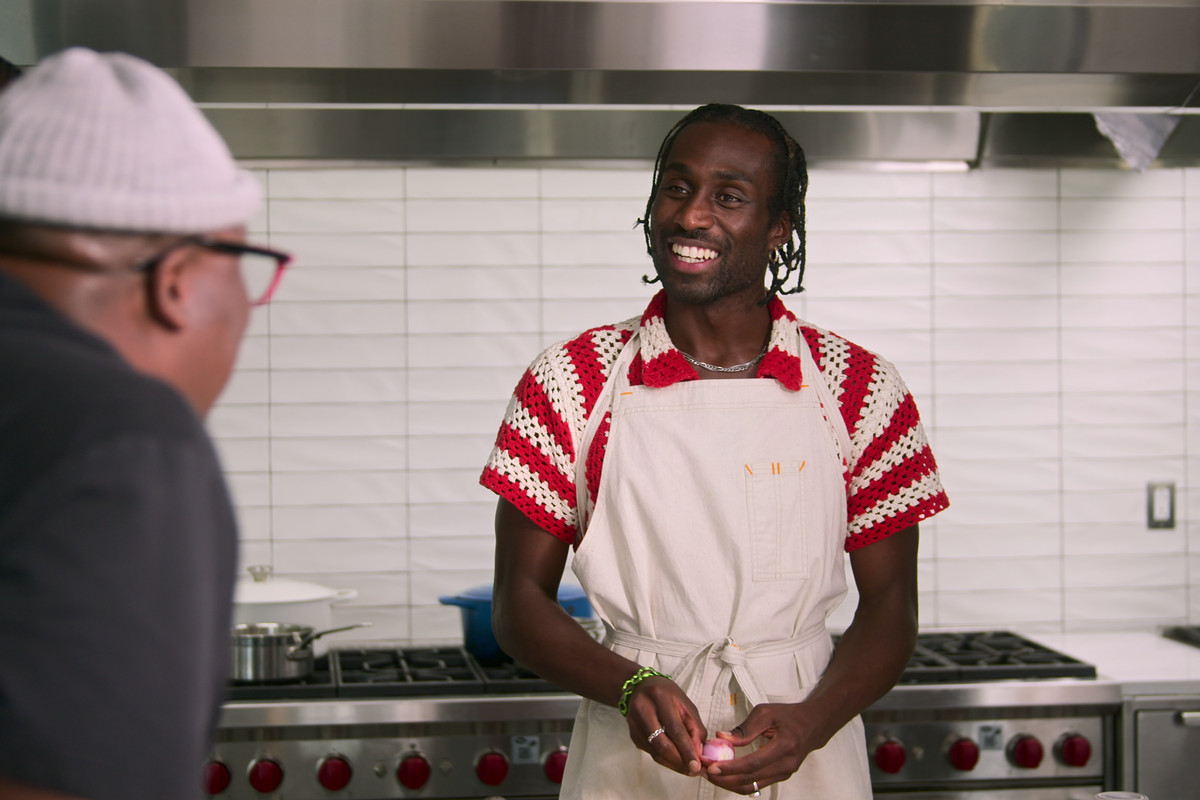 A person wearing an apron and a red-and-white-striped knit shirt stands in a restaurant kitchen