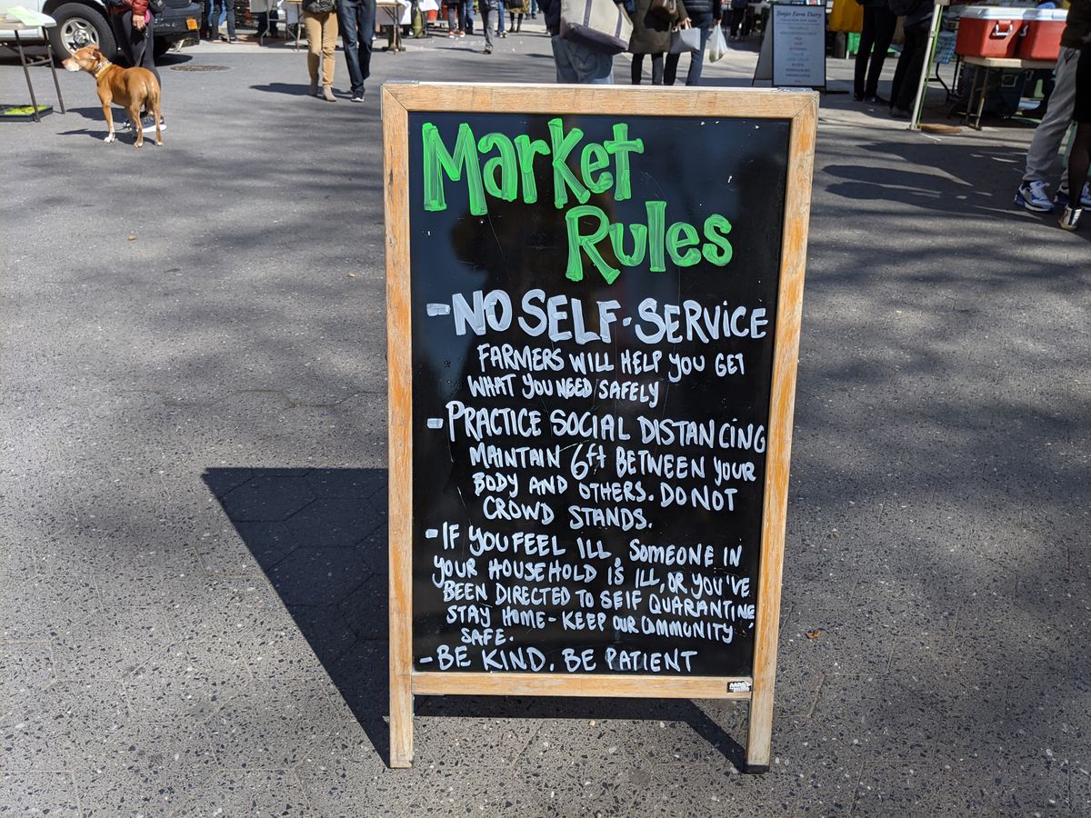 A sign lists rules for shopping at the greenmarket, including maintaining safe distances apart.