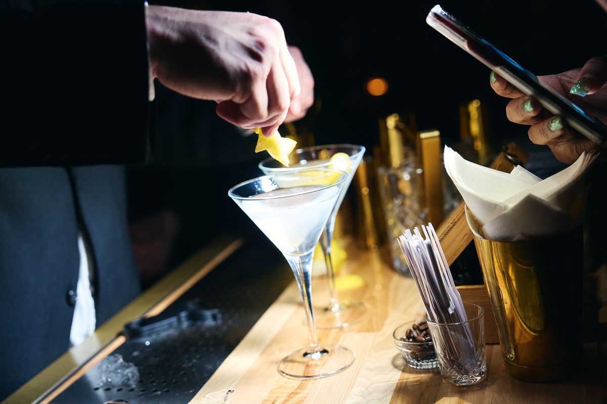 A bartender spritzes lemon zest on a martini.