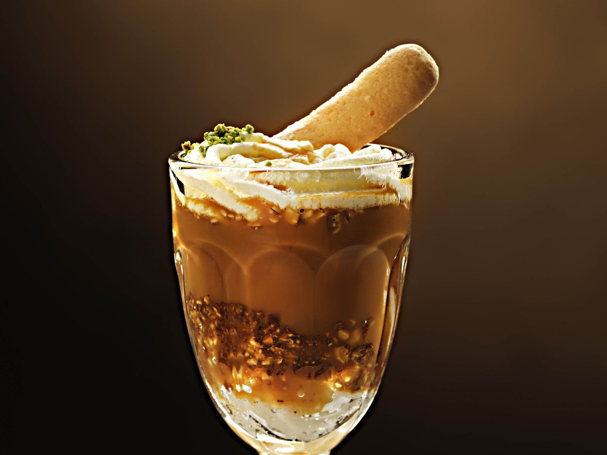 An ornate glass filled with ice cream, caramel, and topped with an oblong piece of brittle.