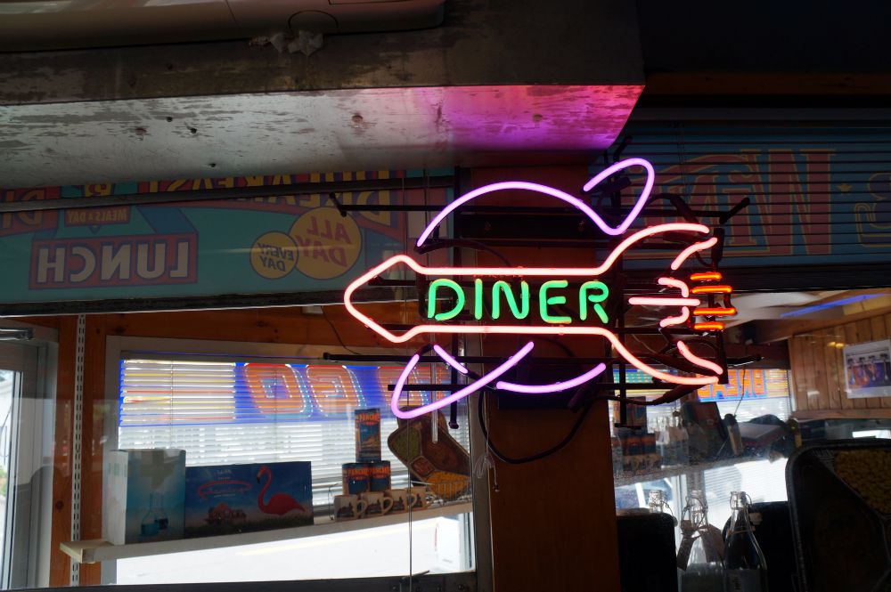 Closeup shot inside a diner showing a neon sign that says “diner” on a rocket ship flying past Saturn