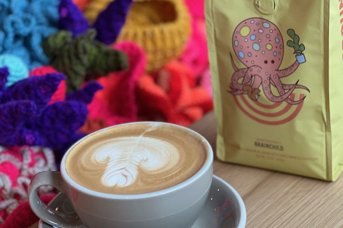 A latte in a ceramic mug positioned next to one of Wunderground’s coffee blends with a cartoon octopus on the bag. 