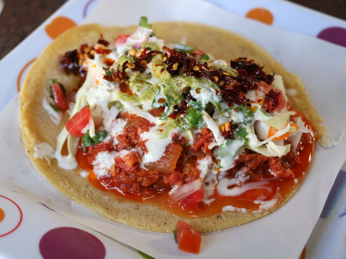A taco covered in three sauces and fixings lying on a napkin on top of a colorfully dotted paper plate