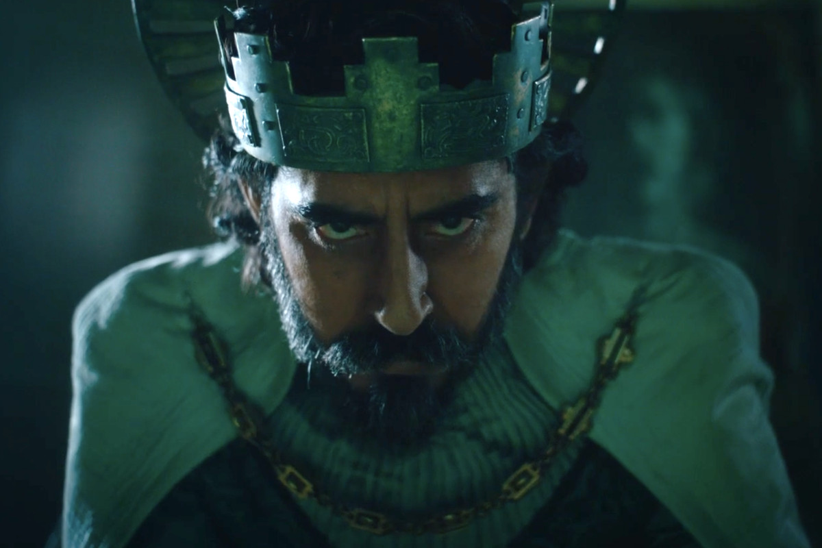Dev Patel wears robes and a crown, and a pained expression.