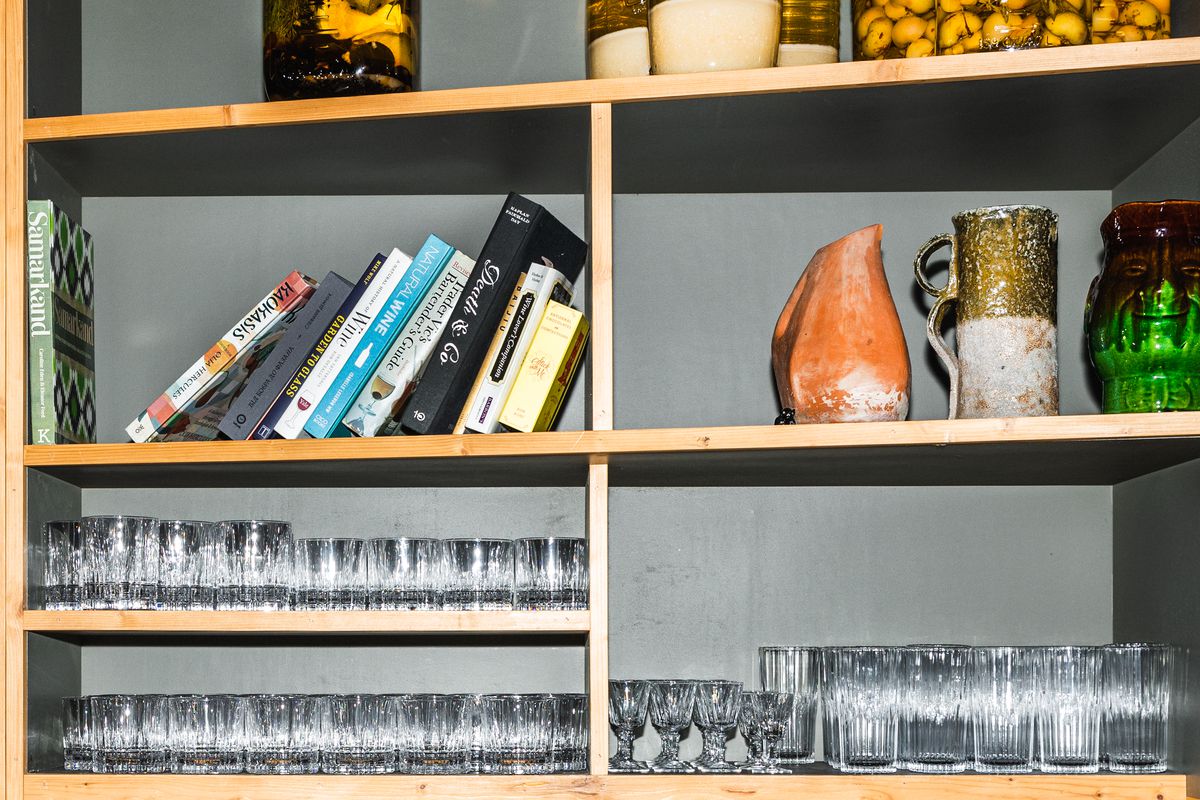A shelf display of glasses, cookbooks, and ceramic vessels.