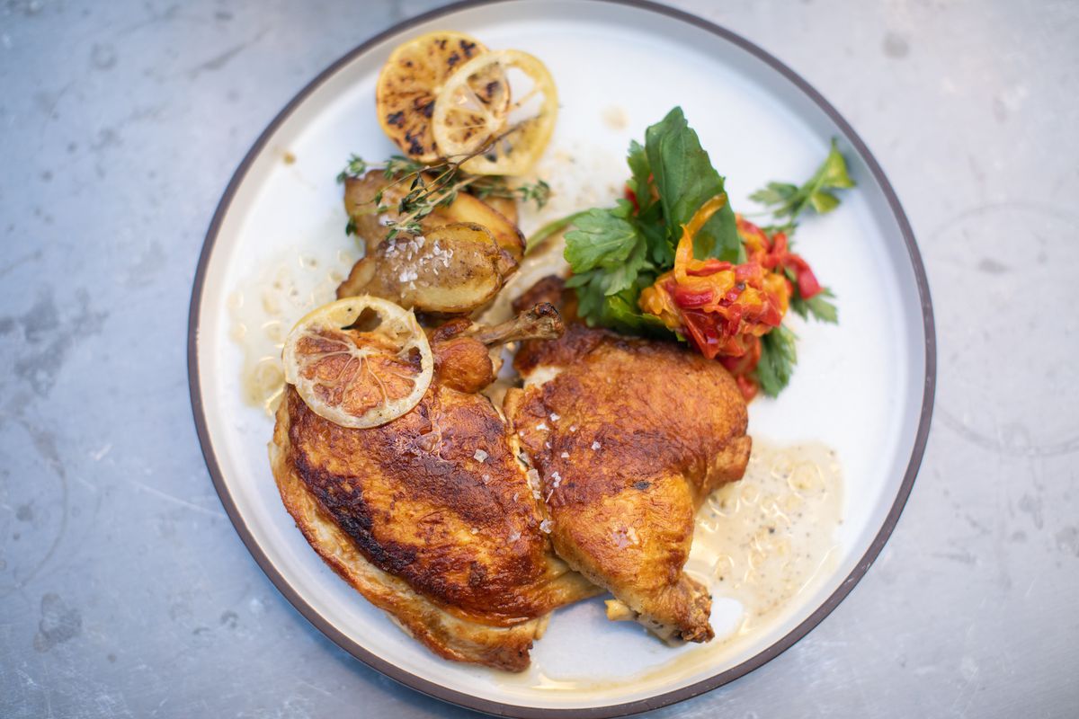 A flattened fried chicken with slices of charred lemon scattered over the top.