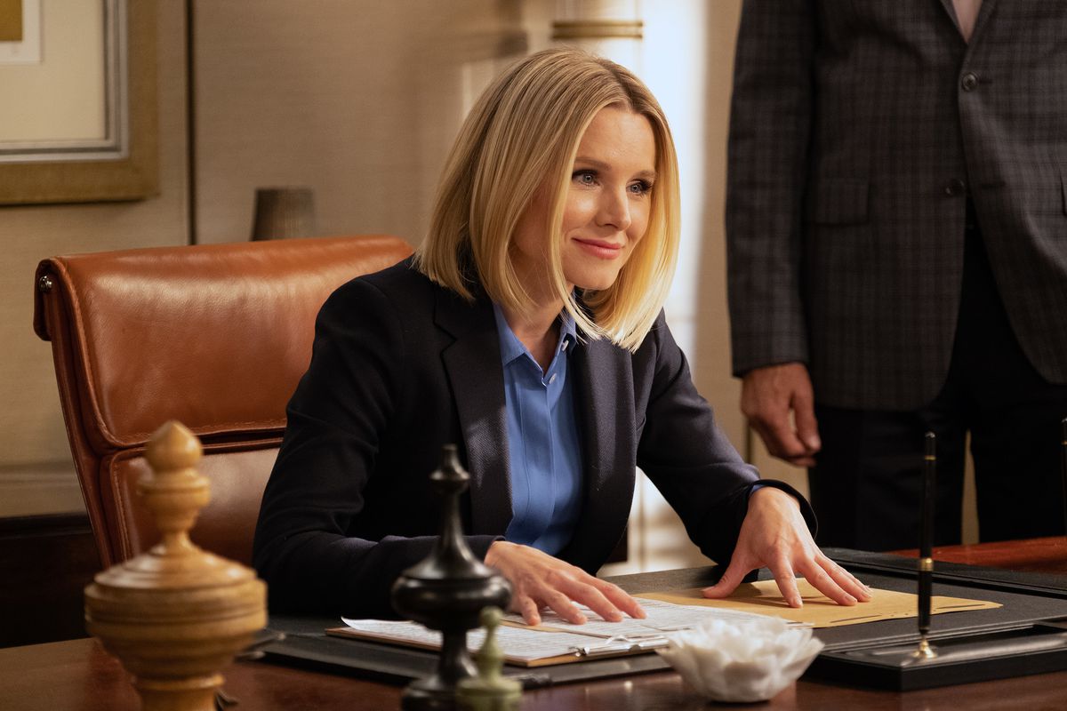 Kristen Bell as Eleanor in “The Good Place” sits at a desk and smiles.
