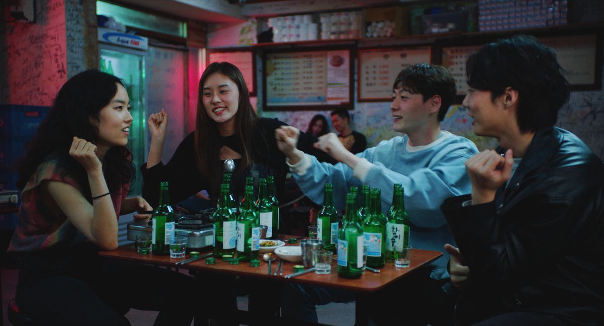 A group of four Korean young people sits around a table littered with beer bottles.