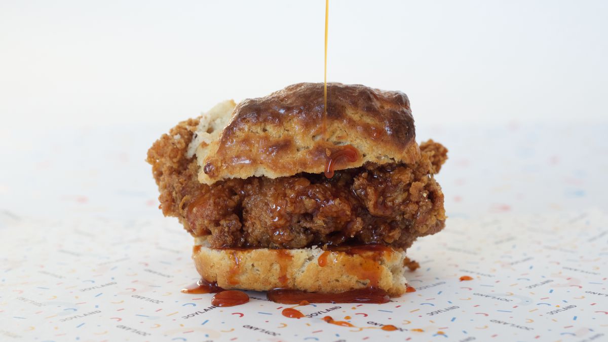 close up of fried chicken biscuit with sauce actively drizzling from above
