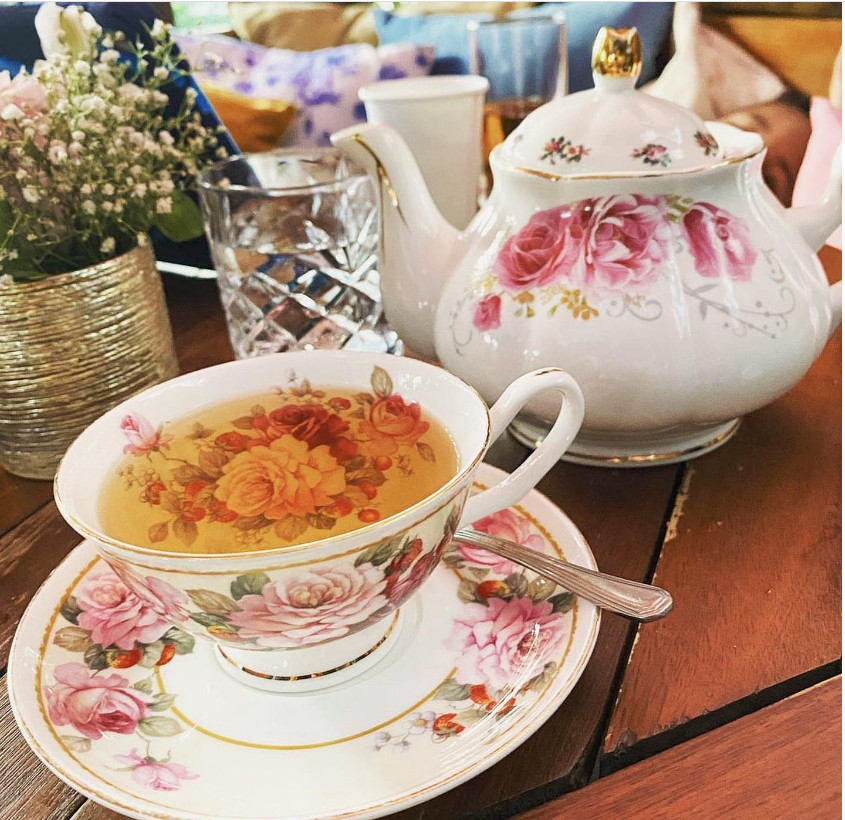 A pink and white floral tea pot with a cup of tea.
