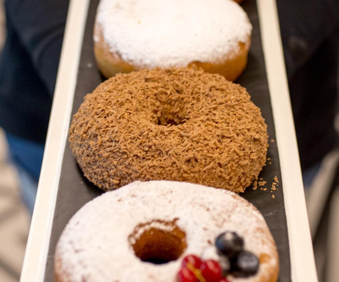 Four donuts of various styles and colors on a tray receding into the background
