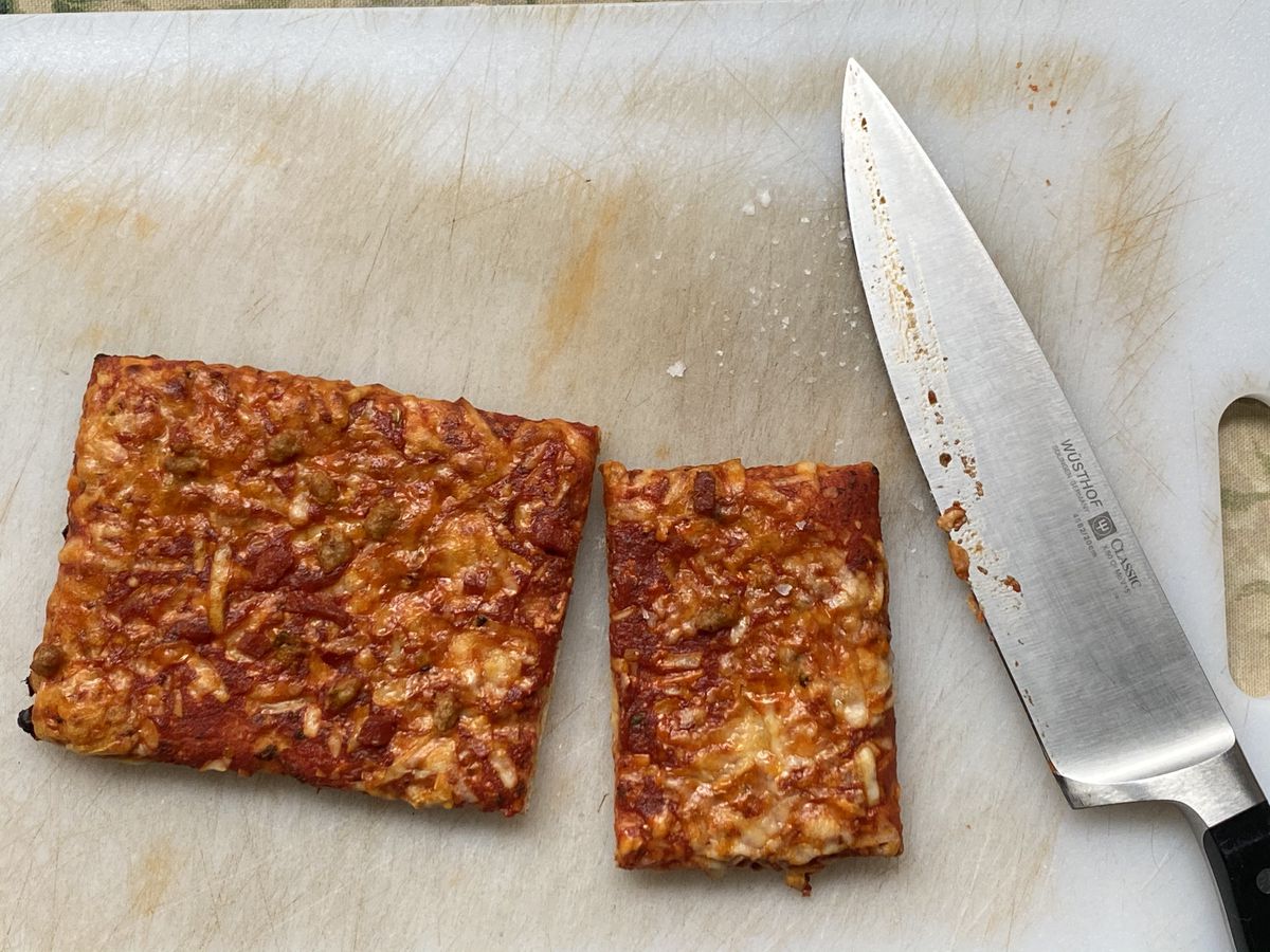 Ellio’s pizza, partially cut, sits next to a Wusthof knife and a scattered pile of fleur de sel