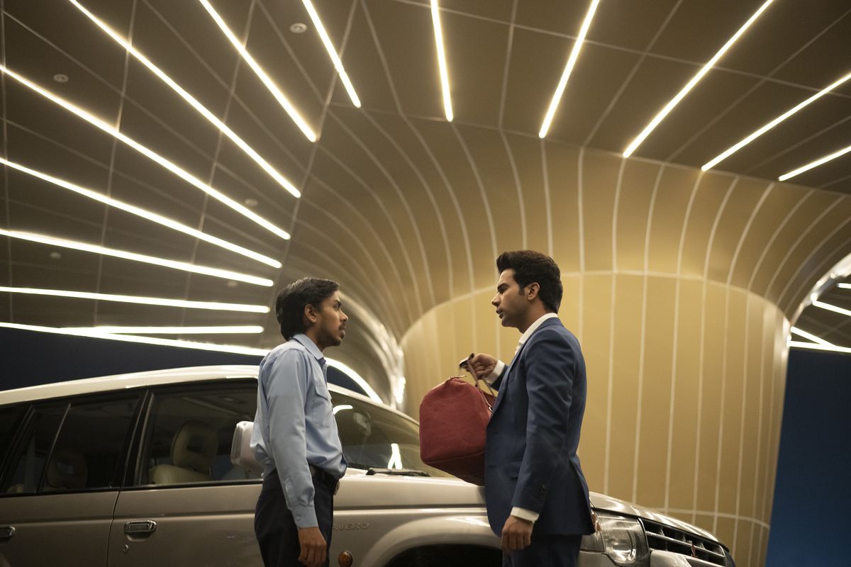 Adarsh ​​Gourav and Rajkummar Rao face each other in The White Tiger under a carport striped with neon lights.