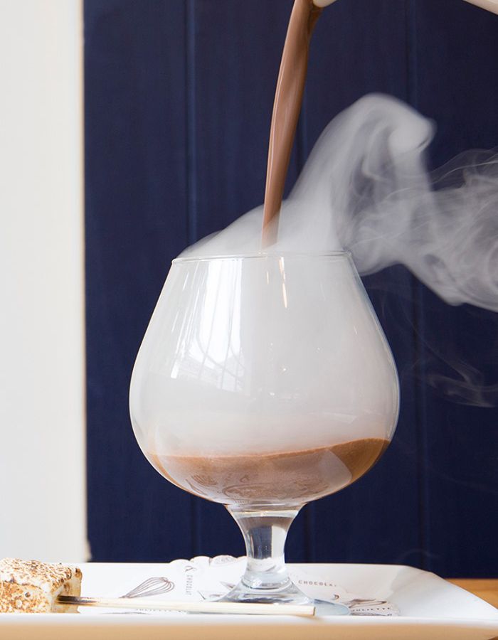 Steaming hot chocolate is poured into a brandy balloon glass.