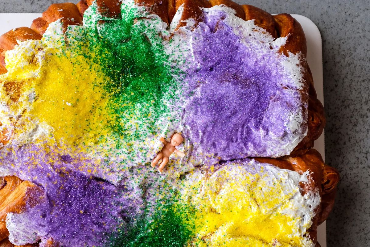 Overhead shot of a croissant-like cake covered in white icing with yellow, green, and purple sprinkles.