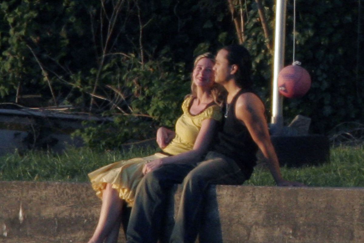 A couple sitting on a sunny concrete wall and leaning back on a grassy verge.
