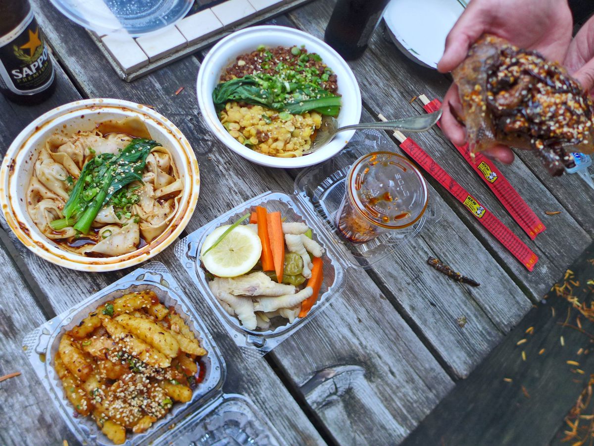 A wooden table outdoors seen from above with Chinese food spread across it.