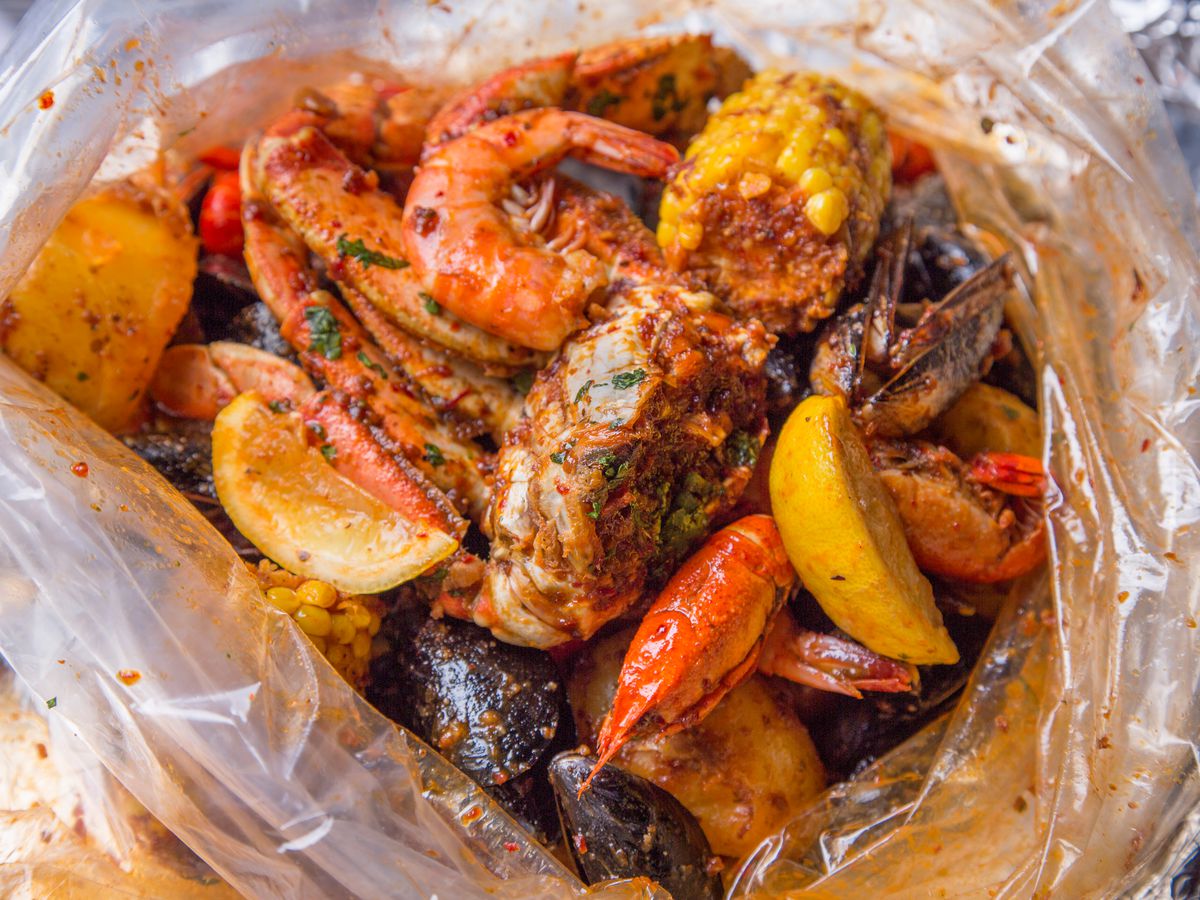 A plastic bag filled with a Cajun seafood boil of corn, shrimp, mussels, lemon wedges, and more.
