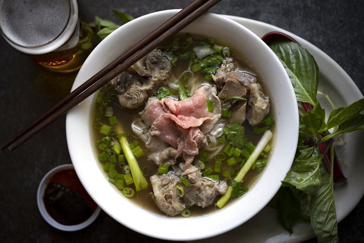 A bowl of broth, chunks of oxtail, rare thin-sliced steak, and green onion.