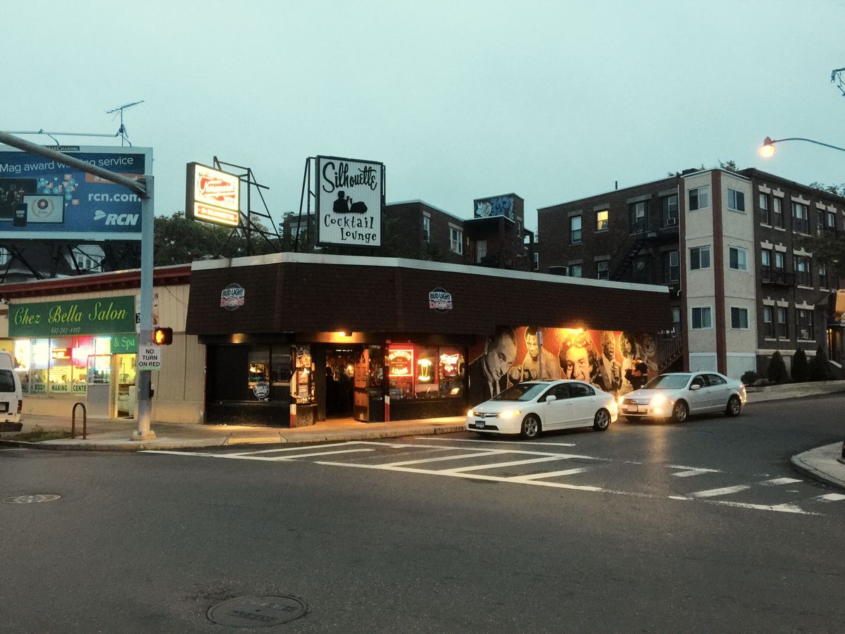 The exterior of a dive bar on the corner of a city street at dusk. Signage reads Silhouette in black cursive, and a colorful mural is painted over one side of the bar’s dark exterior.