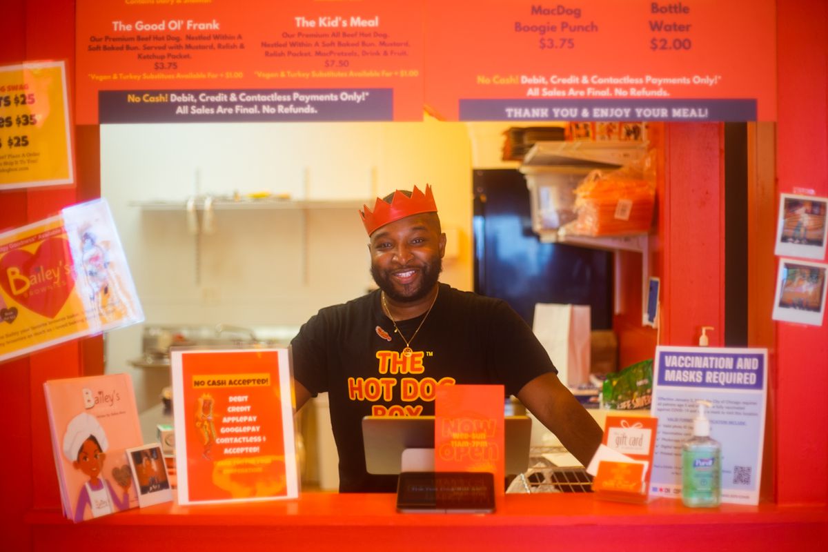 A man wearing a red crown poses and smiles behind a red restaurant counter.