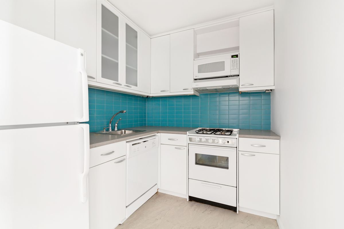 A kitchen with white cabinetry and bright blue tiles.