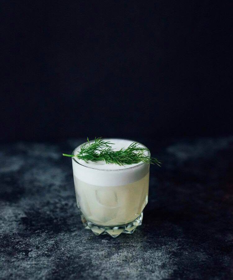 A white cocktail with a frothy top and dill on top.