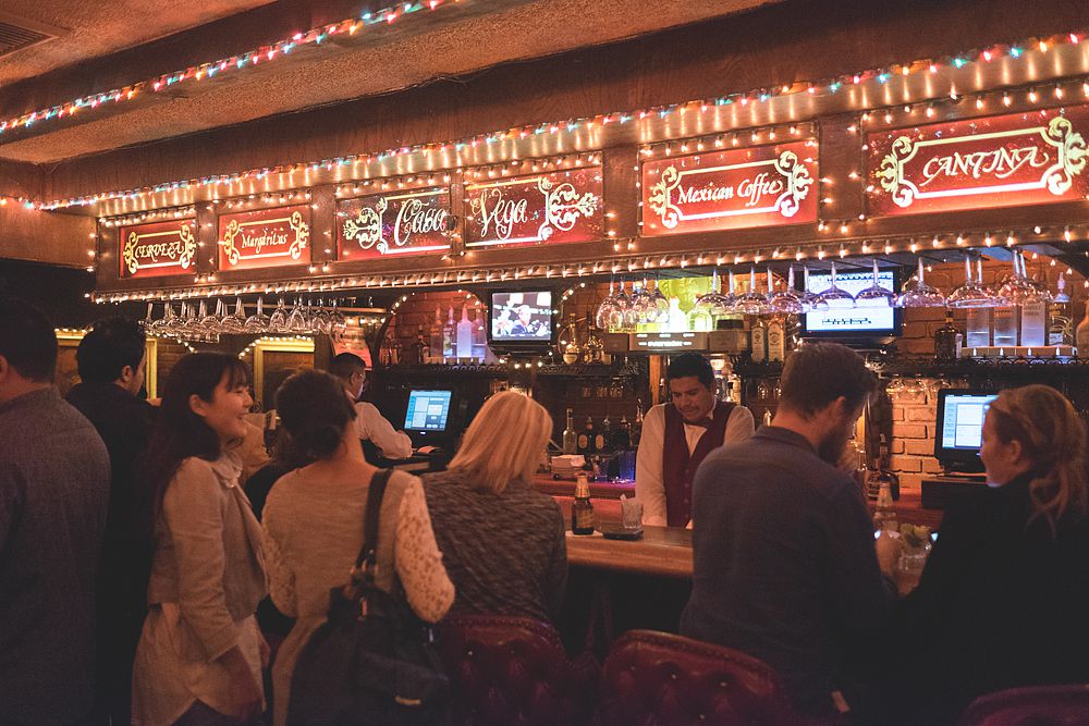 A view of a the very crowded bar at Casa Vega, which has neon signs that say “Mexican Coffee” and “Cantina.”