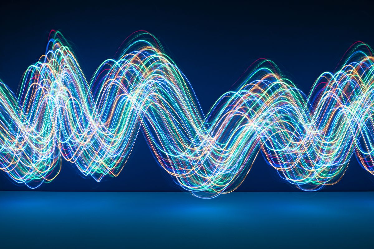 Multi-colored abstract flowing light trails make sine waves against a dark blue background.