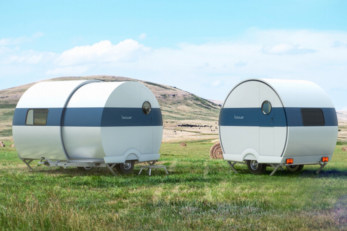 Two silver, semi-circle camper trailers sit in a field of grass. On the left the camper is expanded while on the right the camper is smaller.