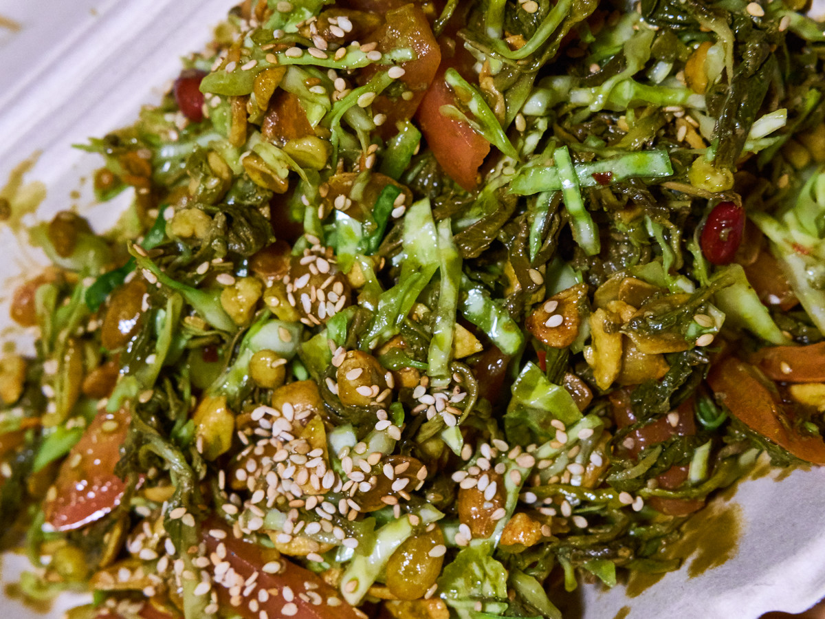 A brightly colored tea leaf salad, with tomatoes, nuts, and seeds.