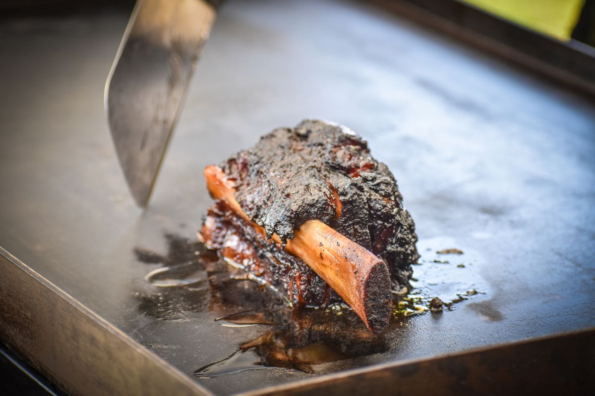 A spatula turns a thick beef rib with lots of dark crust on top of a flat-top griddle at a restaurant pop-up.