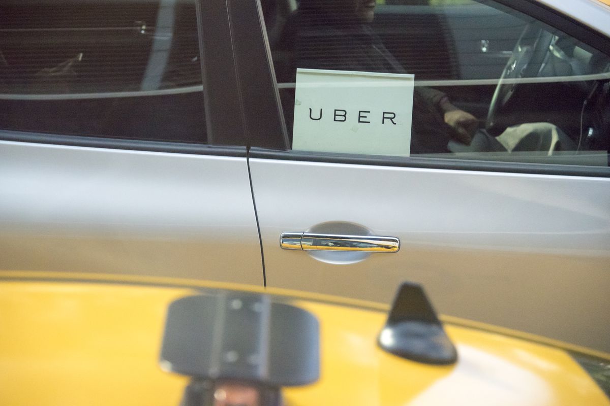 A car with an Uber sign in the window beside a yellow taxi