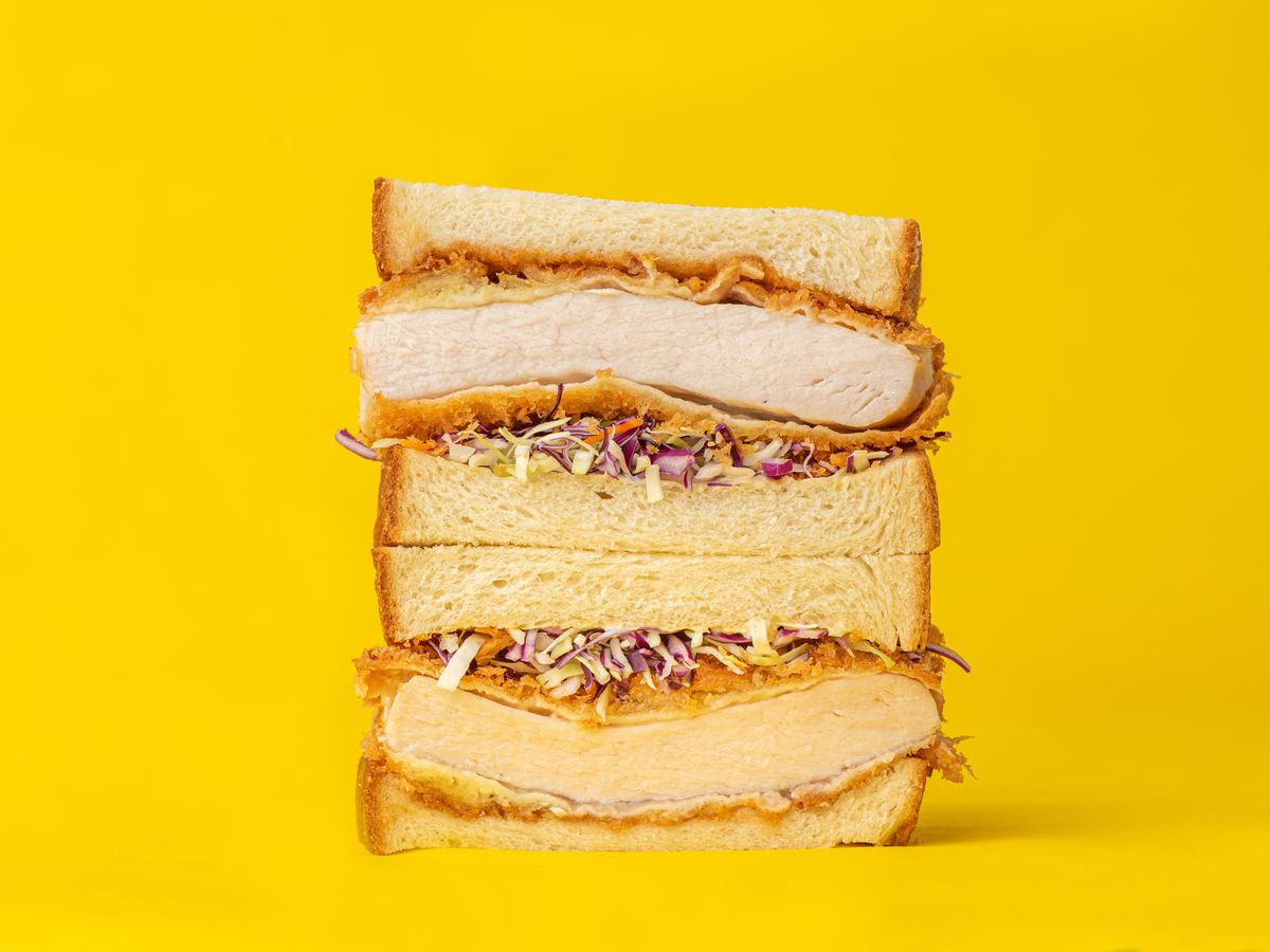 A pork katsu sandwich stacked high with a yellow background.