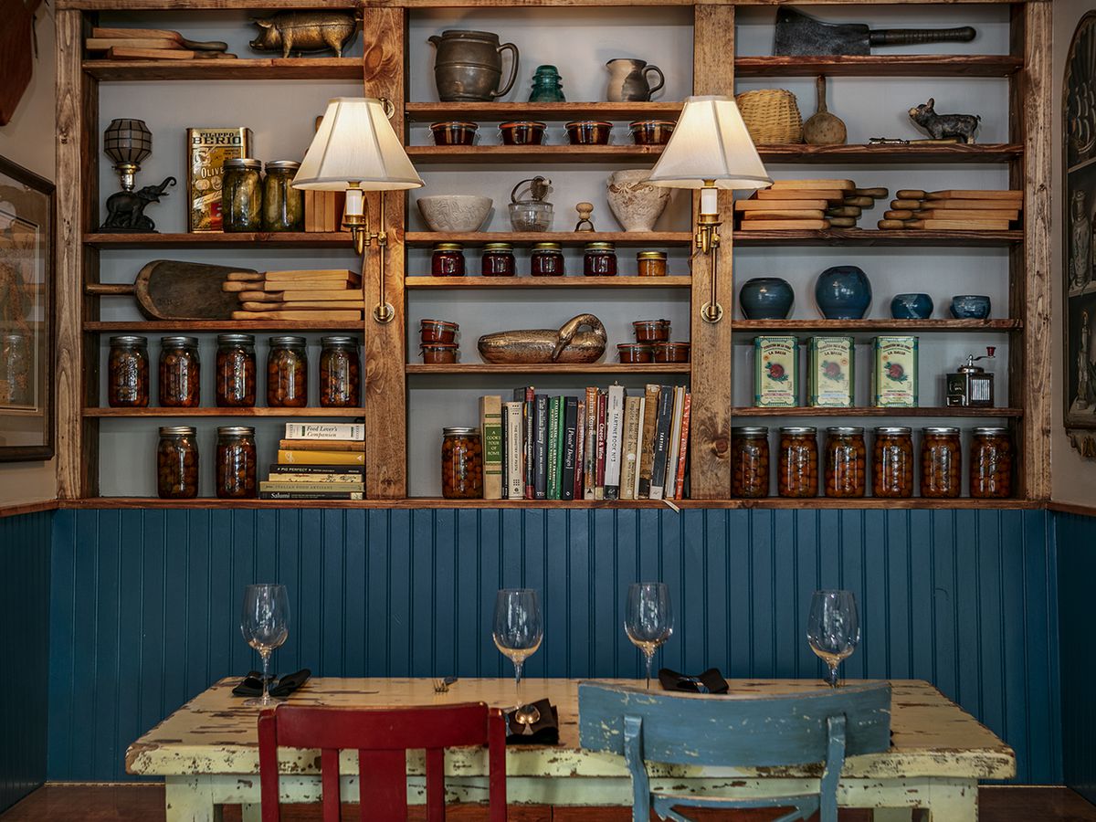 A table with peeling painted chairs sits in front of a bookcase full of old books, with walls and shelves painted teal.