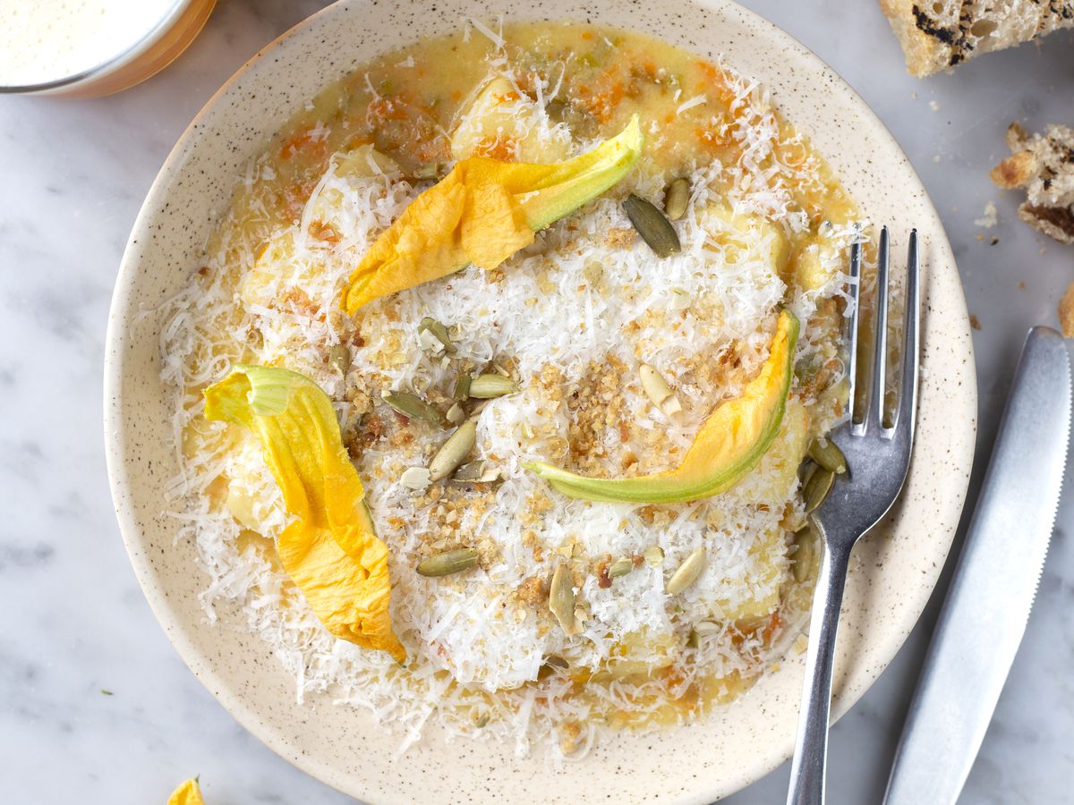 A wide bowl of gnocchi topped with cheese and squash blossoms. 