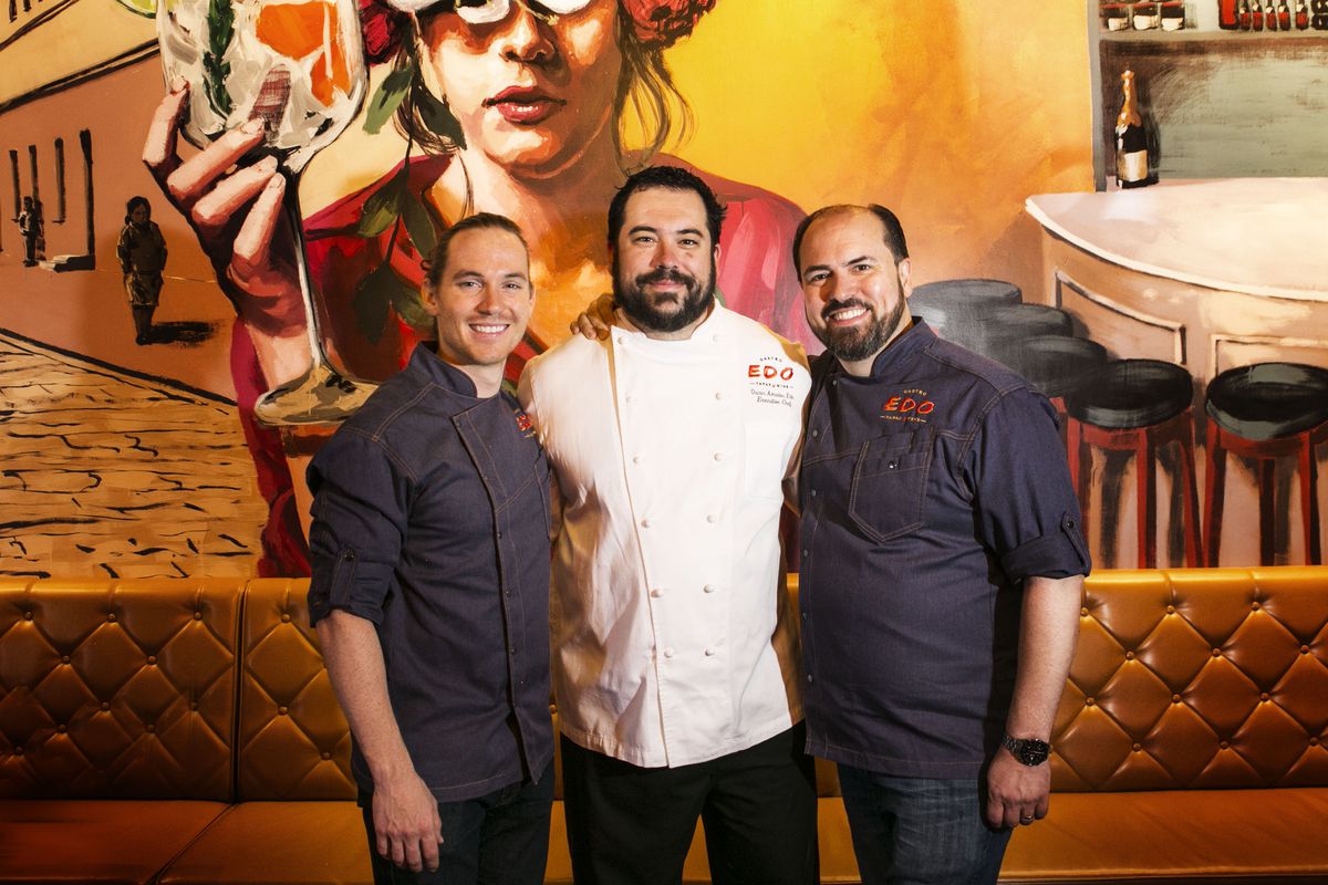 Three men stand in front of a mural at a Spanish restaurant