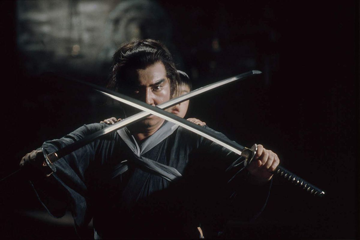 Ronin warrior Ogami Ittō crossing two swords in front of himself with his son Daigorō on his back in  Lone Wolf and Cub: Baby Cart at the River Styx.