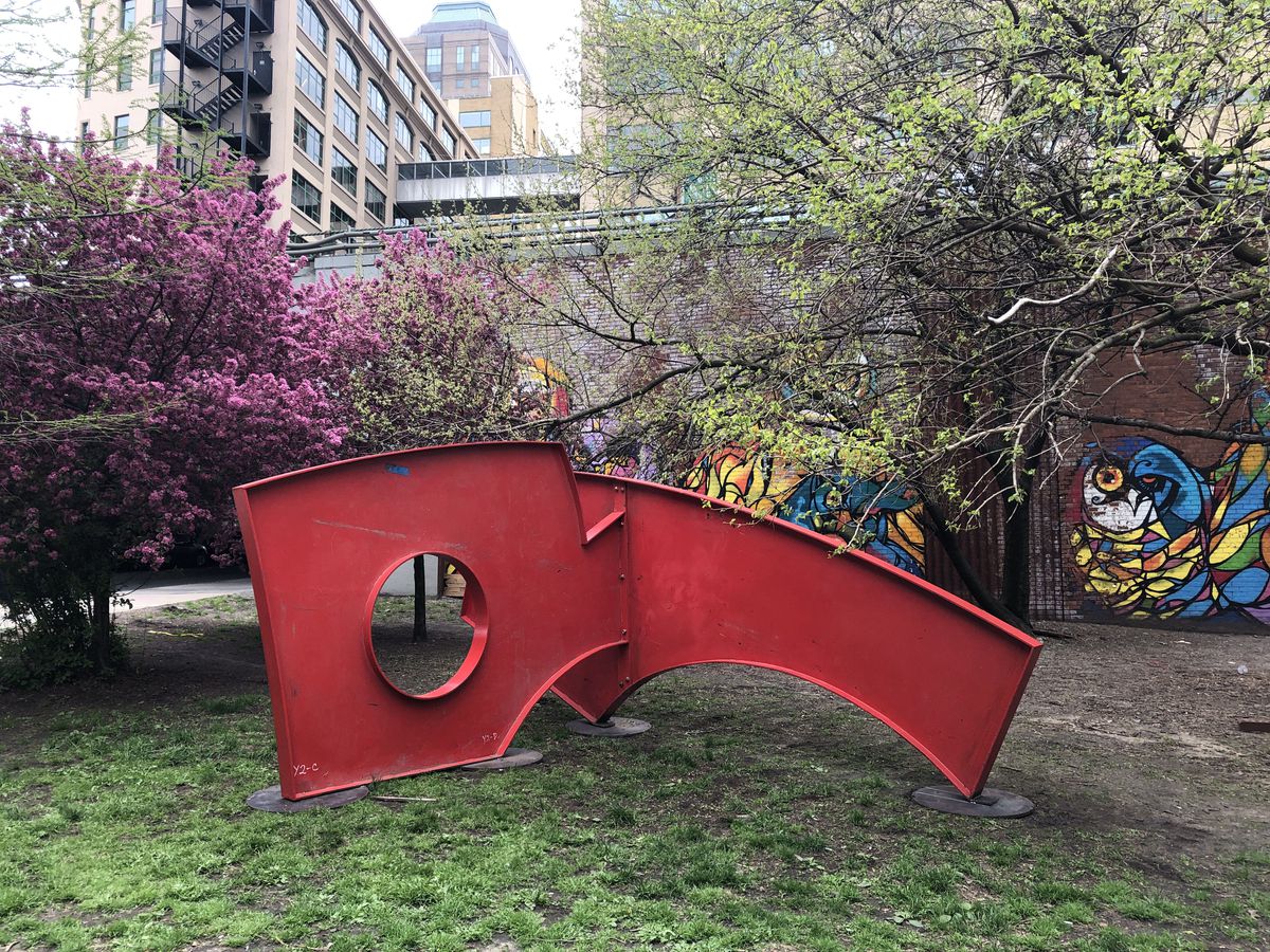 A red figure installed in a park, made out of recycled steel. 