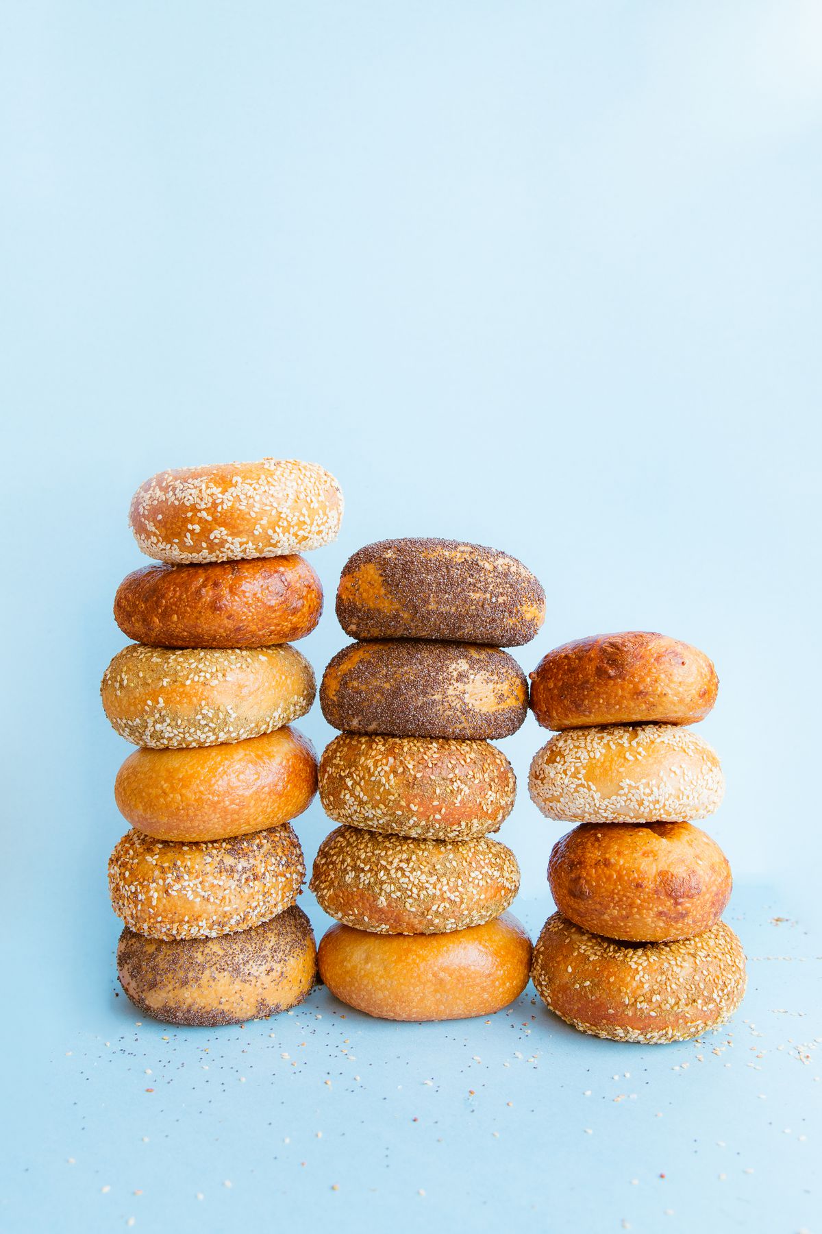 Three stacks of bagels, the tallest with six bagels stacked on top of each other, on a light blue surface.