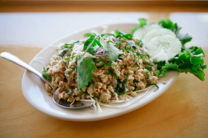 A white plate holds ground meat topped with sprigs of cilantro and garnished with cucumber slices on a leaf of lettuce.