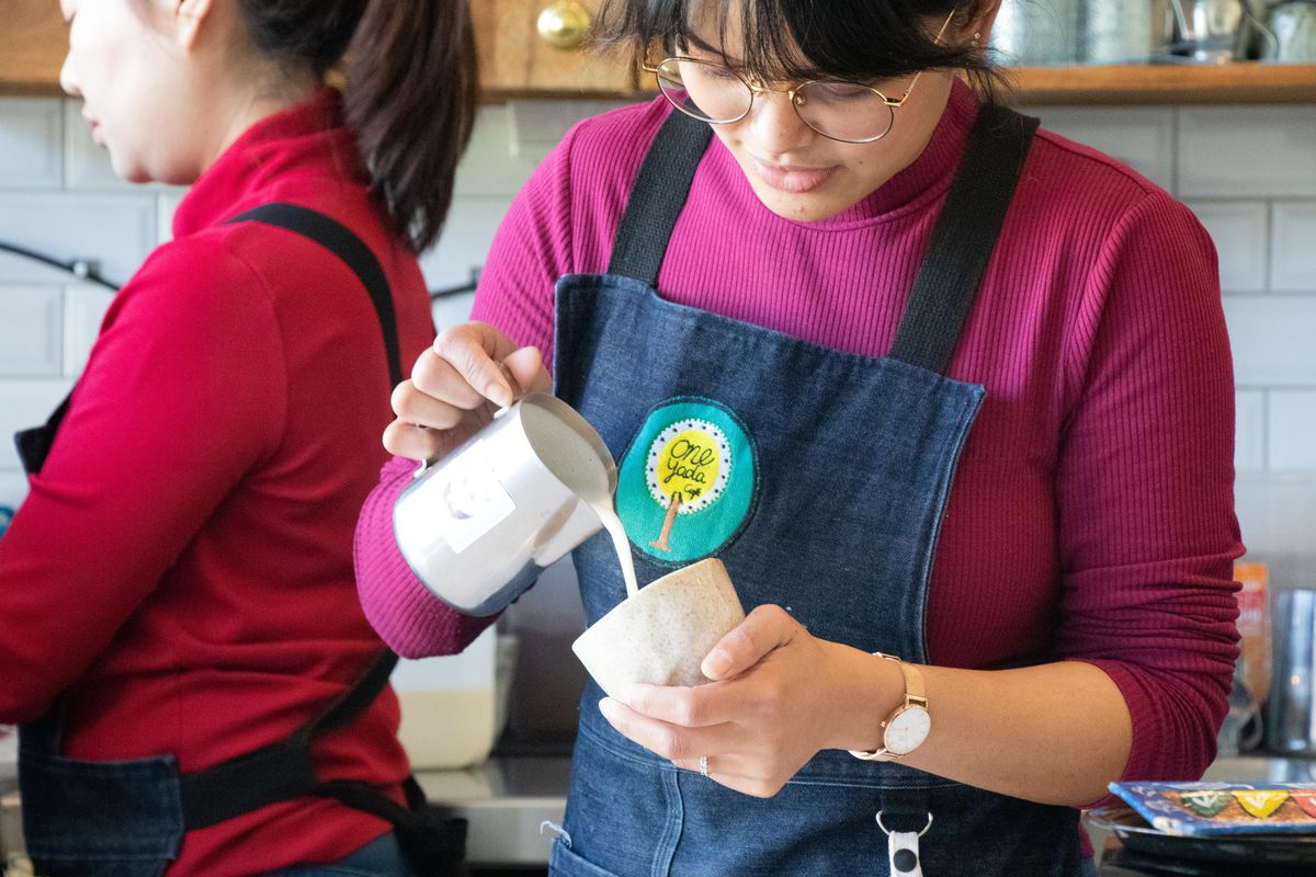 A person wearing an apron pours milk into a mug