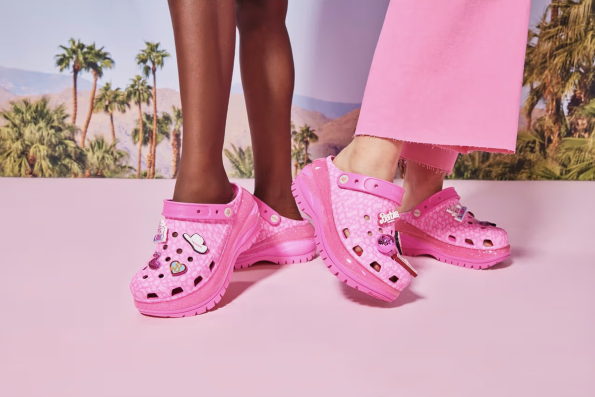 A Black person and a white person modeling the new Barbie Crocs.