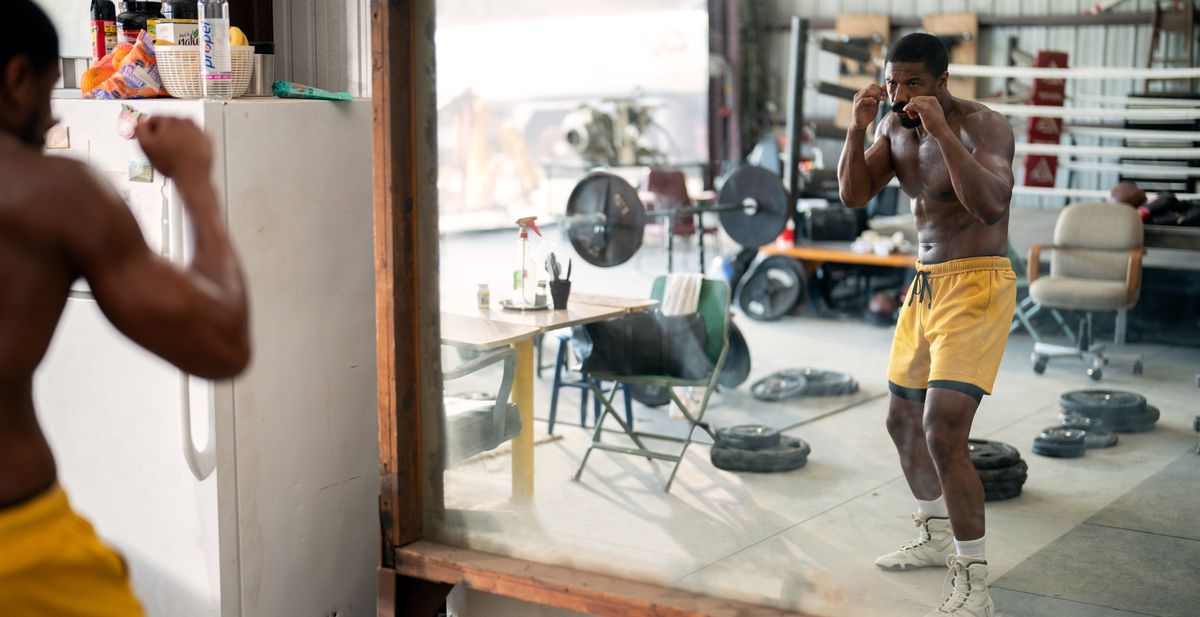 Adonis Creed (Michael B. Jordan), in yellow boxing trunks, faces off against himself in a mirror in Creed III, as if to say “You know what I’m really fighting in this movie? Myself.”