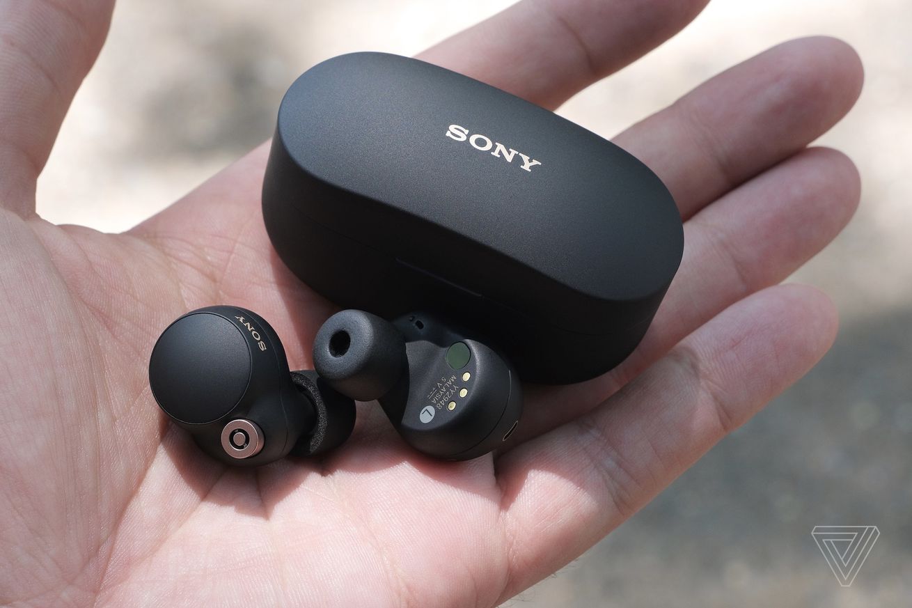 Sony WF-1000XM4 earbuds and their charging case held in the palm of a hand.