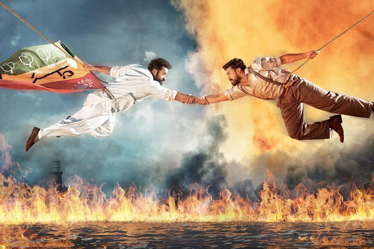 A scene from RRR with two men flying at each other through the air, fire in the background.