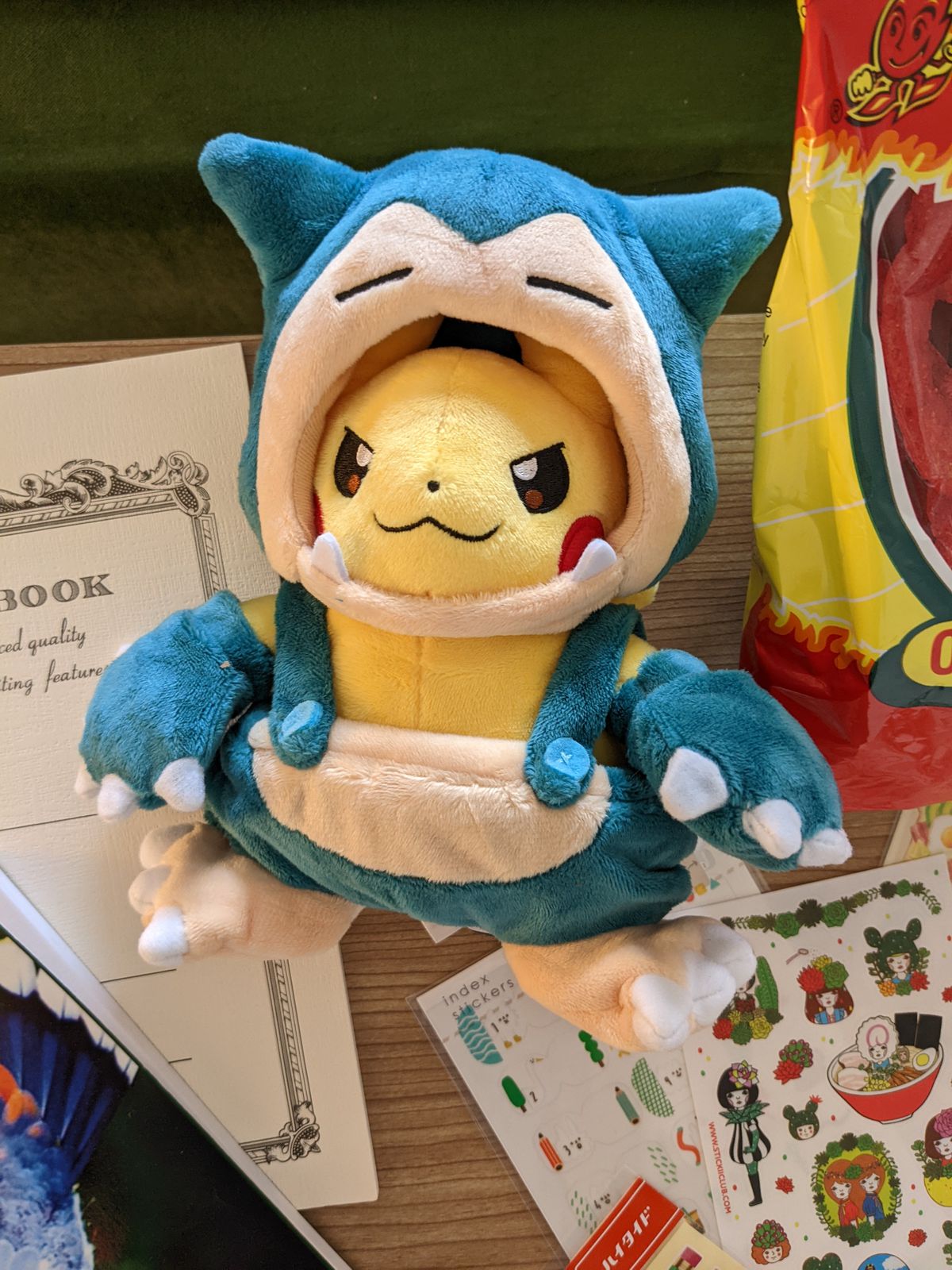 A photo of a plushie Pikachu wearing a Snorlax costume