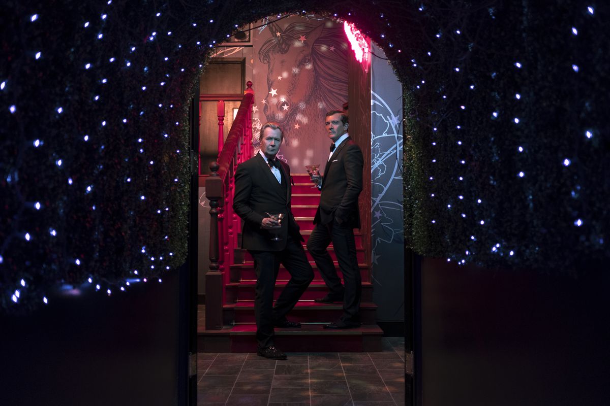 Jürgen Mossack (Oldman) and Ramón Fonseca (Banderas), clad in tuxedos, stand on a staircase.