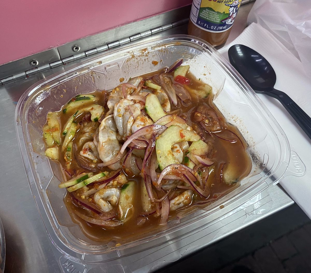 Red juices, red onion, cucumber, and pieces of seafood slosh around in a plastic container.