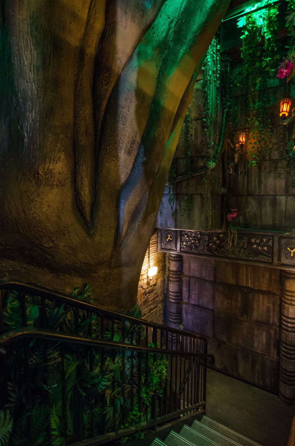 A large fake tree and dangling vines, plus a stone wall, decorate a restaurant stairwell.